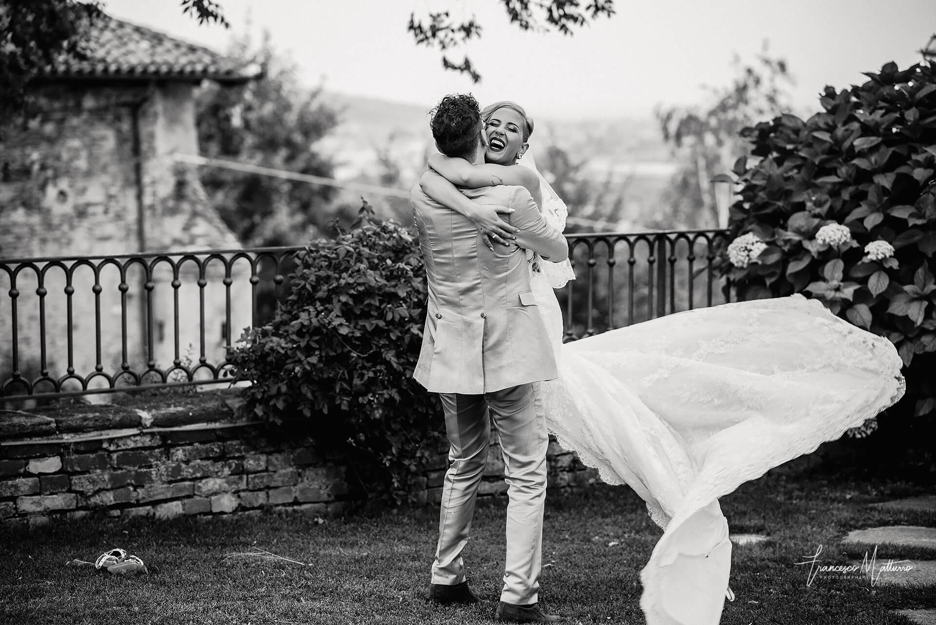 Fotografo di matrimonio Asti - foto in bianco e nero di due sposi che si stringono in un abbraccio, lui solleva lei e la fa volteggiare mentre sorride nel parco del castello rosso di costigliole saluzzo di Francesco Matturro